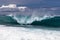 Hawaiian wave curling, aboung to hit the sea. Foam in foreground; clouds in background.