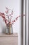 Hawthorn branches with red berries in vase on wooden table indoors