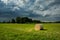 Hay bale, green meadow and dark clouds