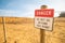 Hazard warning sign. You cannot go beyond this border. Desert. Barbed wire. Blue sky and light white clouds. A very gloomy picture