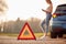 Hazard Warning Triangle Sign For Car Breakdown On Road With Woman Calling For Help In Background