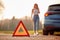 Hazard Warning Triangle Sign For Car Breakdown On Road With Woman Calling For Help In Background