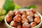 Hazelnuts in a round green bowl with green leaves close-up on a wooden table. Farmed ripe hazelnuts. Nut abundance