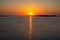 Hazy sun rising above houses on a barrier island, reflecting in a bay.