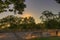 HDR image of a sun setting down in the evening behind the trees in a park with comfortable old benches in the foreground
