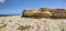 HDR panorama photo of a sunny day at the sea coast with deep blue clean water and a nice stone beach and a large rock on the right