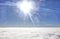 HDR photo of an airplane wing against the blue sky with a cloud cover underneath and brigh shining sun in in front of it