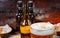 Head of beer foam in glass near bottles and plates with pistachios, small pretzels, peanuts on dark wooden desk