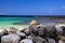 Head of blonde woman with straw hat sitting behind wall of piled natural rocks on beach with turquoise ocean