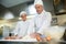 Head chef showing smiling trainee how to prepare dough