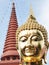 Head of golden Buddha statue and top of brown mosaic finished pagoda with blue sky background