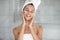 Head shot relaxed woman applying moisturizing face cream after shower