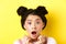 Head shot of shocked asian girl with hairbuns and glamour makeup, open mouth and looking startled at camera, standing