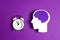 Head silhouette with a purple brain and white alarm clock on a purple background