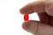 Headache pain relief, pharmaceutical treatment and sickness fighting concept with close up fingers holding red gel capsule