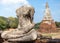 Headless and armless statue of Buddha seated in lotus position made of stone, stupa made of brick behind. Thai Buddhist temple in