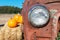 Headlight of abandoned and rusty car with several pumpkin laying on hay bale