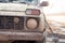 Headlight, grille and bumper of an SUV in mud closeup on the river bank