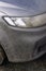 Headlight, hood and bumper of car covered with dirt, vertical photo