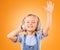 Headphones, happy or child streaming music to relax with freedom in studio on orange background. Hand up, singing or