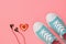 Headphones, red and white heart and turquoise sneakers on pink background. Color trend 2019. Sports style. Flat lay.