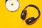 Headphones with a white cable on a yellow background. compact disc player with white cd and earphones