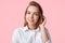 Headshot of adorable female college student with blue eyes, healthy pure skin, wears white shirt, poses against pink background, h