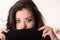 Headshot attractive brunette facing camera covering half her face with black clothing, white studio background