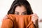 Headshot attractive brunette facing camera covering half her face with orange clothing, white studio background