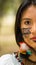 Headshot beautiful Amazonian woman, indigenous facial paint and earrings with colorful feathers, posing seriously for