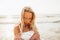 Headshot of beautiful blonde slim girlwearing white dress and cardigan on beach of sea or ocean against the sun. Youth