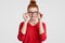 Headshot of beautiful freckled young European woman in eyewear, has gentle smile, dressed in red sweater, rejoices promotion at wo