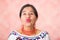 Headshot beautiful hispanic mother wearing traditional andean clothing, making kissing lips to camera, pink studio