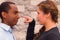 Headshot charming young interracial couple facing each other, she point her finger at his nose, brick wall background