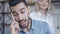 Headshot of cheerful Middle Eastern young man talking on the phone smiling as Caucasian woman passing at background