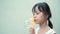 Headshot close-up of a cute girl with long black hair Asian blowing bubbles in front of a white wall background.