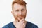 Headshot of creative and intrigued attractive redhead guy with bristle, rubbing beard and smirking, having great plan or