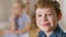 Headshot of cute confident Caucasian brunette boy with blue-grey eyes looking back at blurred girl turning to camera and