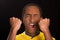 Headshot dark skinned male wearing yellow football shirt in front of black background, eyes closed and mouth open