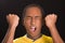 Headshot dark skinned male wearing yellow football shirt in front of black background, eyes closed and mouth open