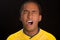 Headshot dark skinned male wearing yellow football shirt in front of black background, eyes closed and mouth open