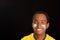 Headshot dark skinned male wearing yellow football shirt in front of black background, flag facial paint, facing camera