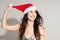 Headshot of joyful cheerful brunette long haired young girl in santa hat on gray studio background with copyspace for ad