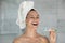 Headshot of laughing woman with towel on head holding toothbrush