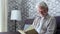 Headshot portrait close up of old happy and relaxed man sitting reading a book at home. Mature male person enjoying free time