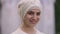 Headshot portrait of gorgeous Middle Eastern bride in white hijab looking at camera smiling standing at wedding altar