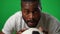 Headshot portrait of perspiring African American sportsman with soccer ball looking at camera on green screen. Close-up