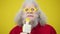 Headshot of positive bearded male retiree in funny eyeglasses singing at microphone on yellow background. Close-up