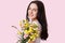 Headshot of pretty European young woman with tender smile, healthy skin, dark long hair, carries bouquet of spring flowers, looks