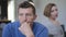 Headshot sad thoughtful adult man looking away as blurred woman looking at spouse turning at background. Close-up upset